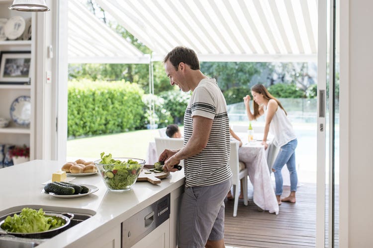 Man making a salad in the kitchen with family on decking