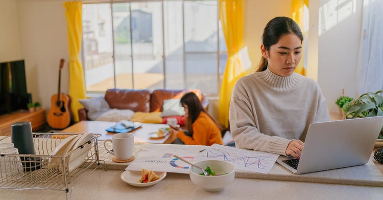 Two women eating and using a laptop and mobile phone at home